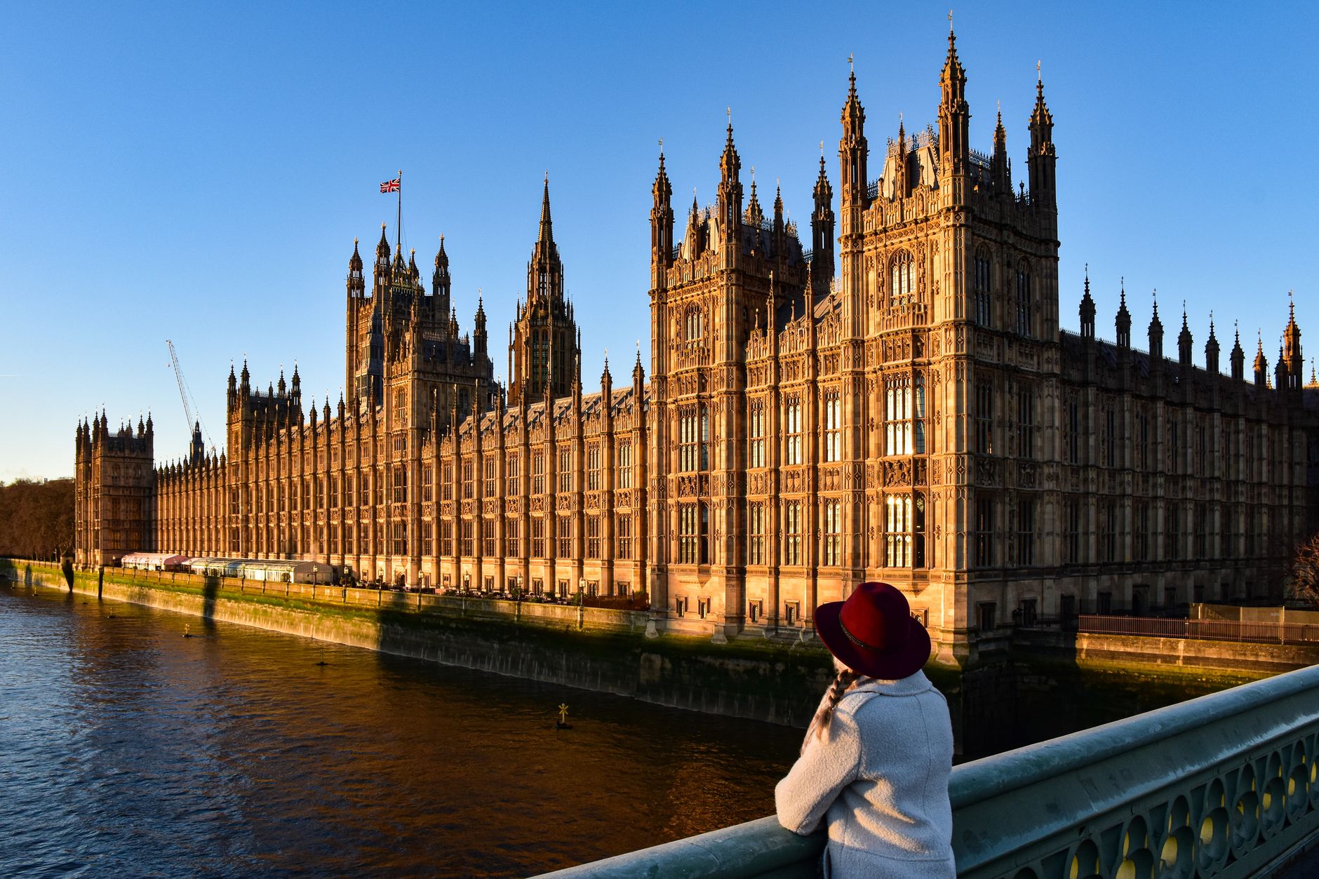 Photograph of Westminster Palace with a person enjoying the view from Westminster Bridge at sunset.