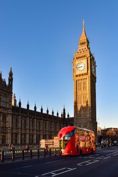 Vibrant red double-decker bus passing by the iconic Big Ben in London during sunset.