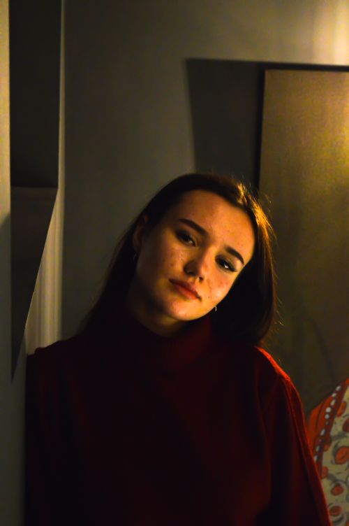 Free A young woman in a dimly lit interior, captured in a moody, reflective pose. Stock Photo