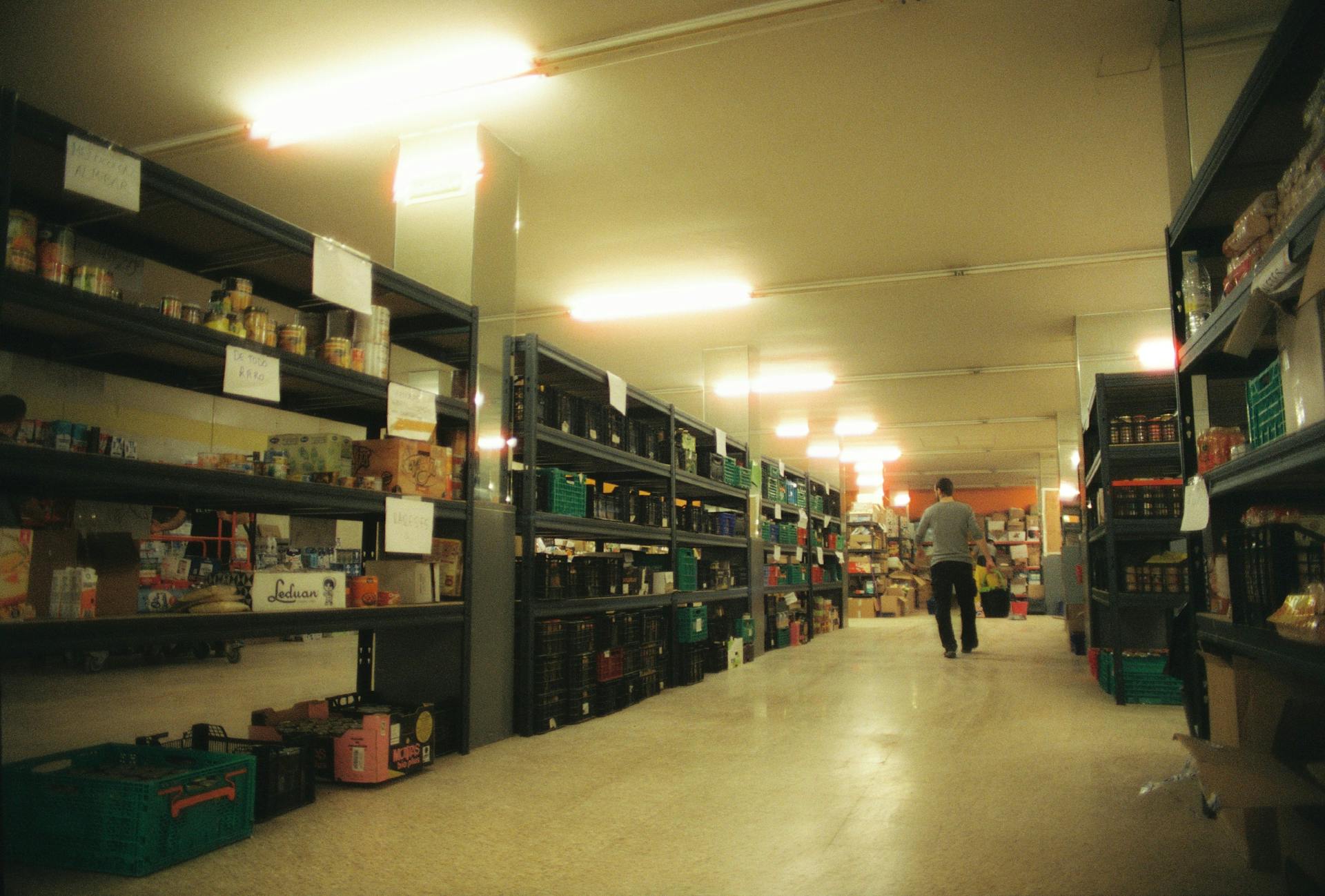 Large warehouse in Alfafar, Spain with shelves stocked with various products and a person walking down the aisle.