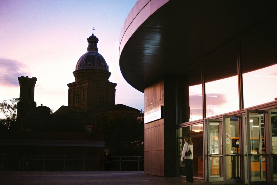 Silhouette of a church dome against a colorful dusk sky near a modern building.