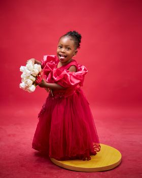 A smiling child in a red dress holding white roses on a vibrant red background.