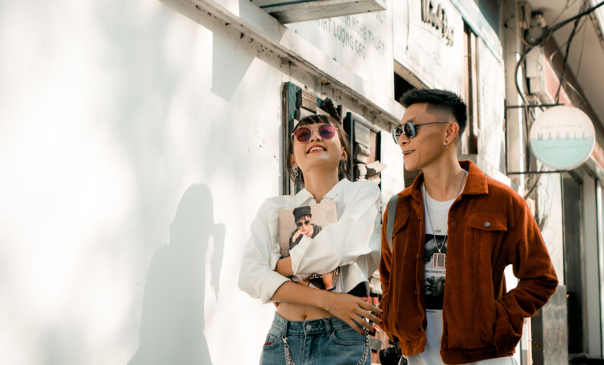 A fashion-forward couple enjoys a sunny walk in stylish outfits, exuding happiness and urban flair.