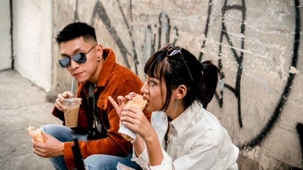 Young urban adults in casual wear enjoying street food outdoors against a graffiti wall.