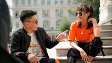 两位时尚的朋友坐在阳光明媚的城市台阶上，笑着享受休闲时光