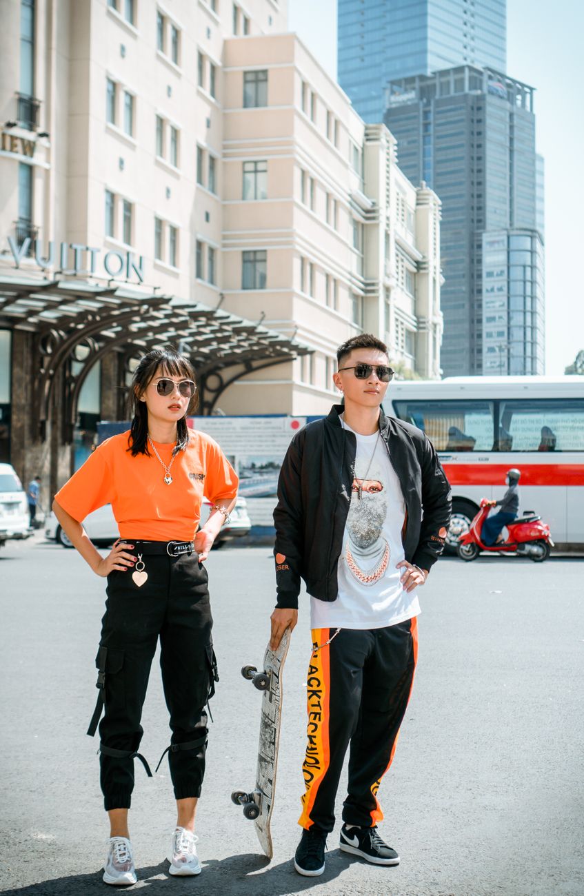 Fashionable young adults pose with skateboard on city street showcasing street style.