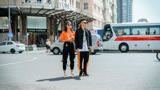 Fashionable couple posing in front of Louis Vuitton store with urban backdrop.