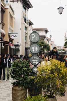 An urban scene with crowds, foliage, and signage directing to amenities.