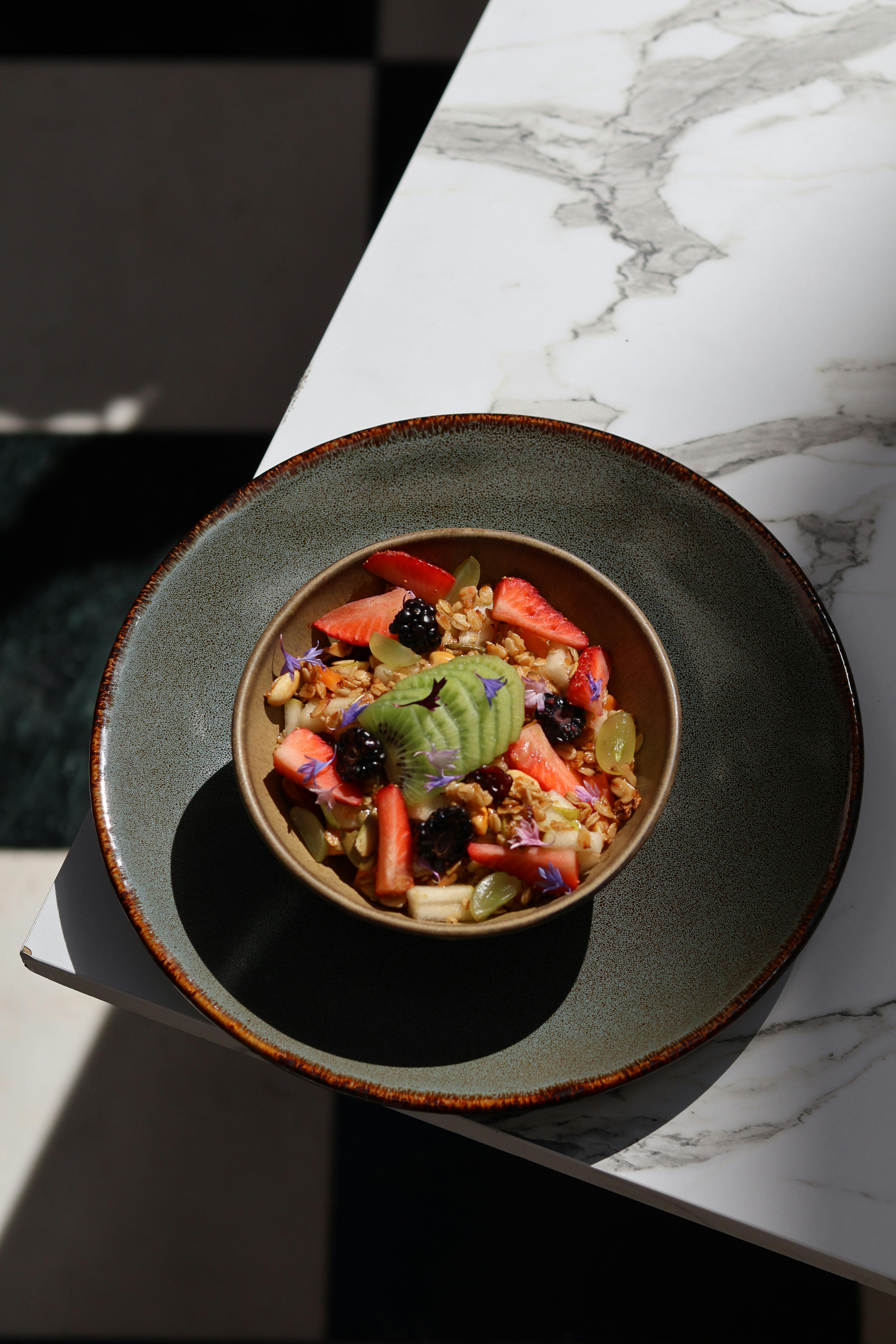 Nutritious breakfast bowl featuring fresh fruits, grains, and edible flowers on a marble surface.