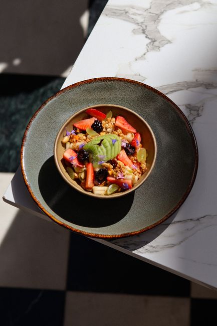 A vibrant bowl of fresh fruit and granola on a marble table illuminated by sunlight.