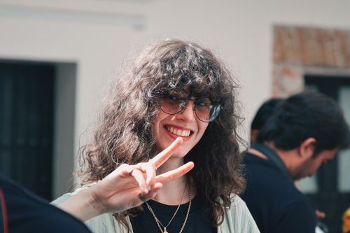 Free Young woman with curly hair flashing a peace sign outdoors, expressing joy. Stock Photo