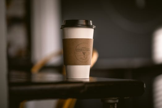 咖啡桌上放着一个带有木套的纸质咖啡杯，背景是模糊的