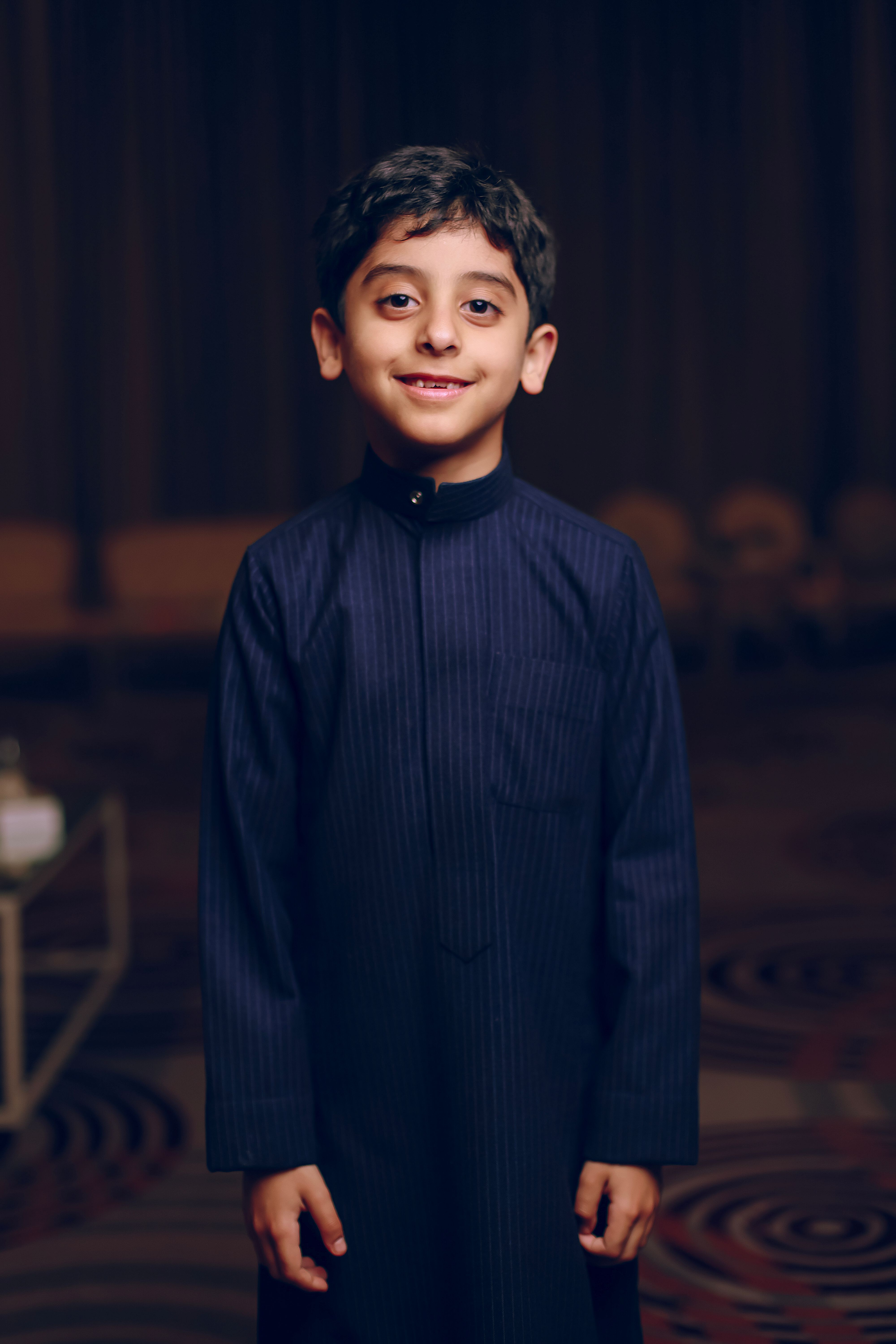 Smiling young boy wearing traditional blue outfit in an indoor setting.