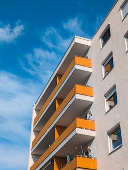 A modern apartment building with distinct orange balconies under a bright blue sky.