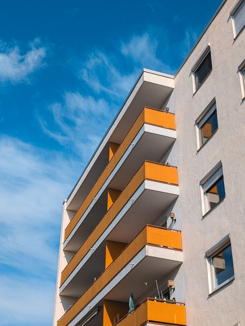 Free A modern apartment building with distinct orange balconies under a bright blue sky. Stock Photo