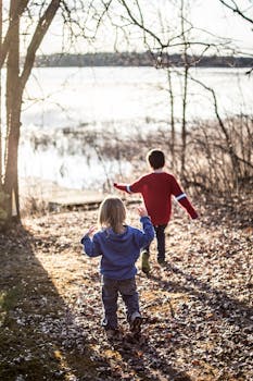 阳光明媚的一天，两个孩子奔跑在湖边森林的小路上
