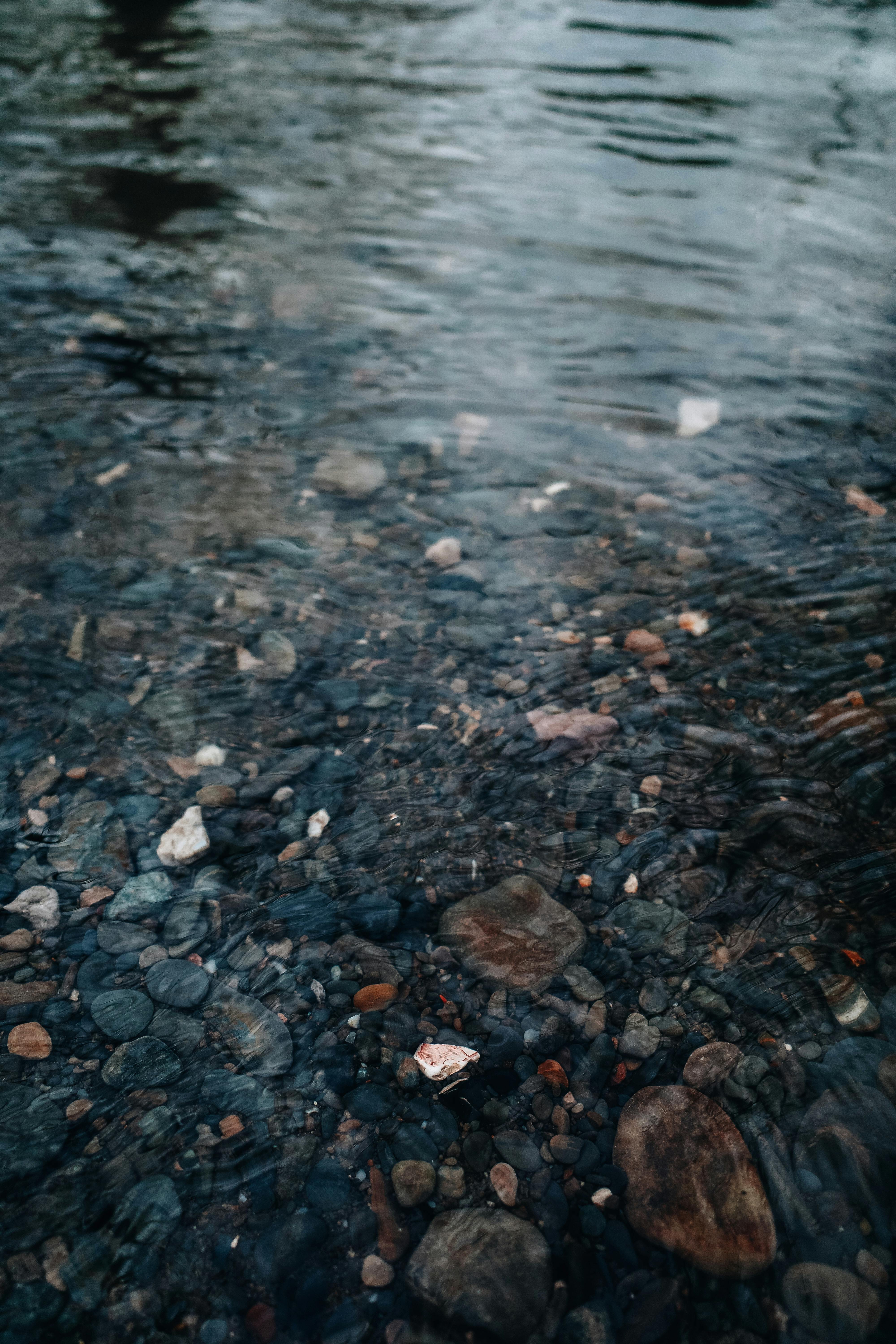 Serene view of a riverbed with smooth pebbles beneath clear water, creating a tranquil natural scene.