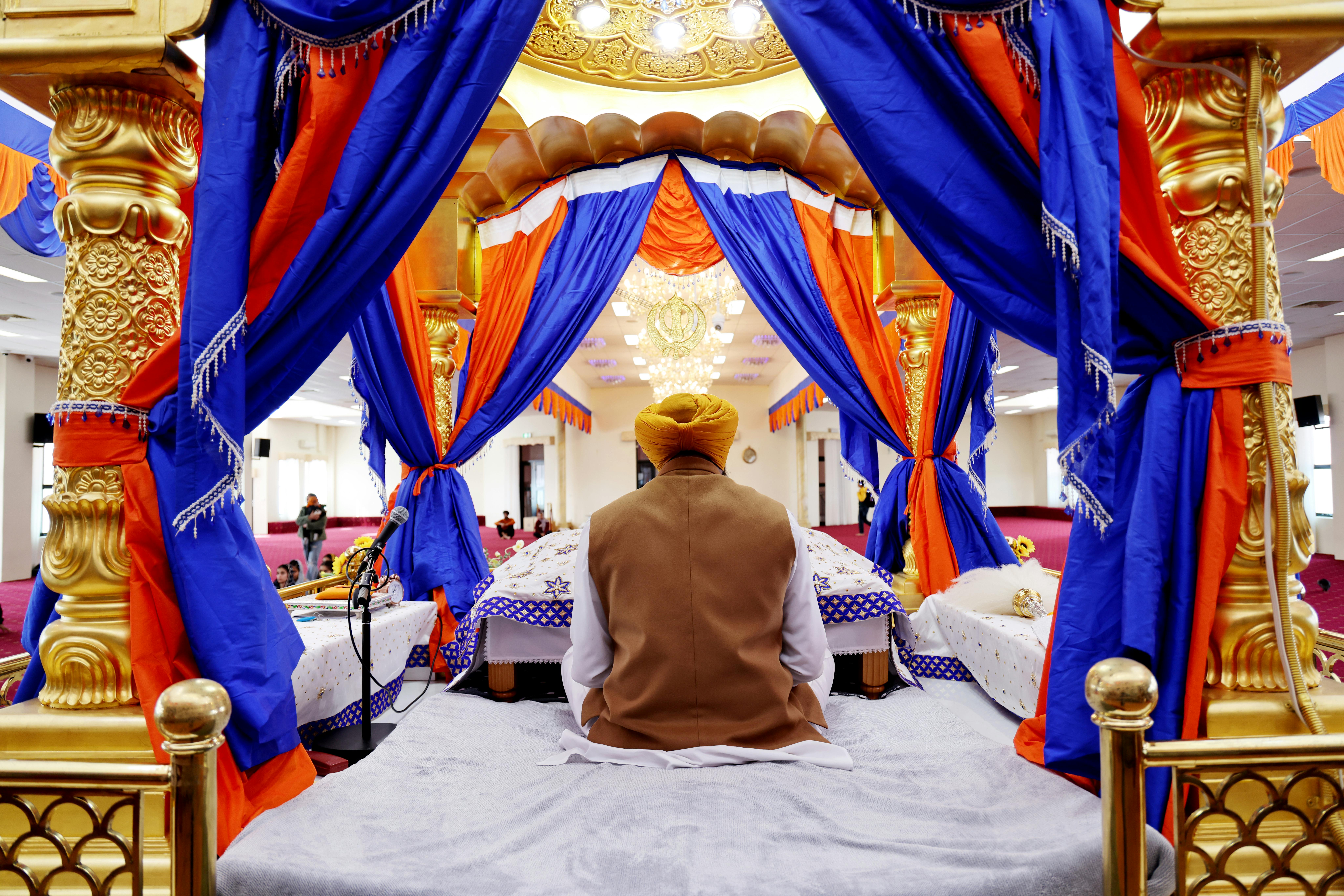 Man seated in Sikh temple, surrounded by vibrant blue and orange drapes, focuses on spirituality.