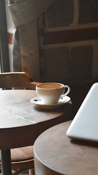 Warm and inviting cafe setting featuring a cup of coffee and laptop on a wooden table.