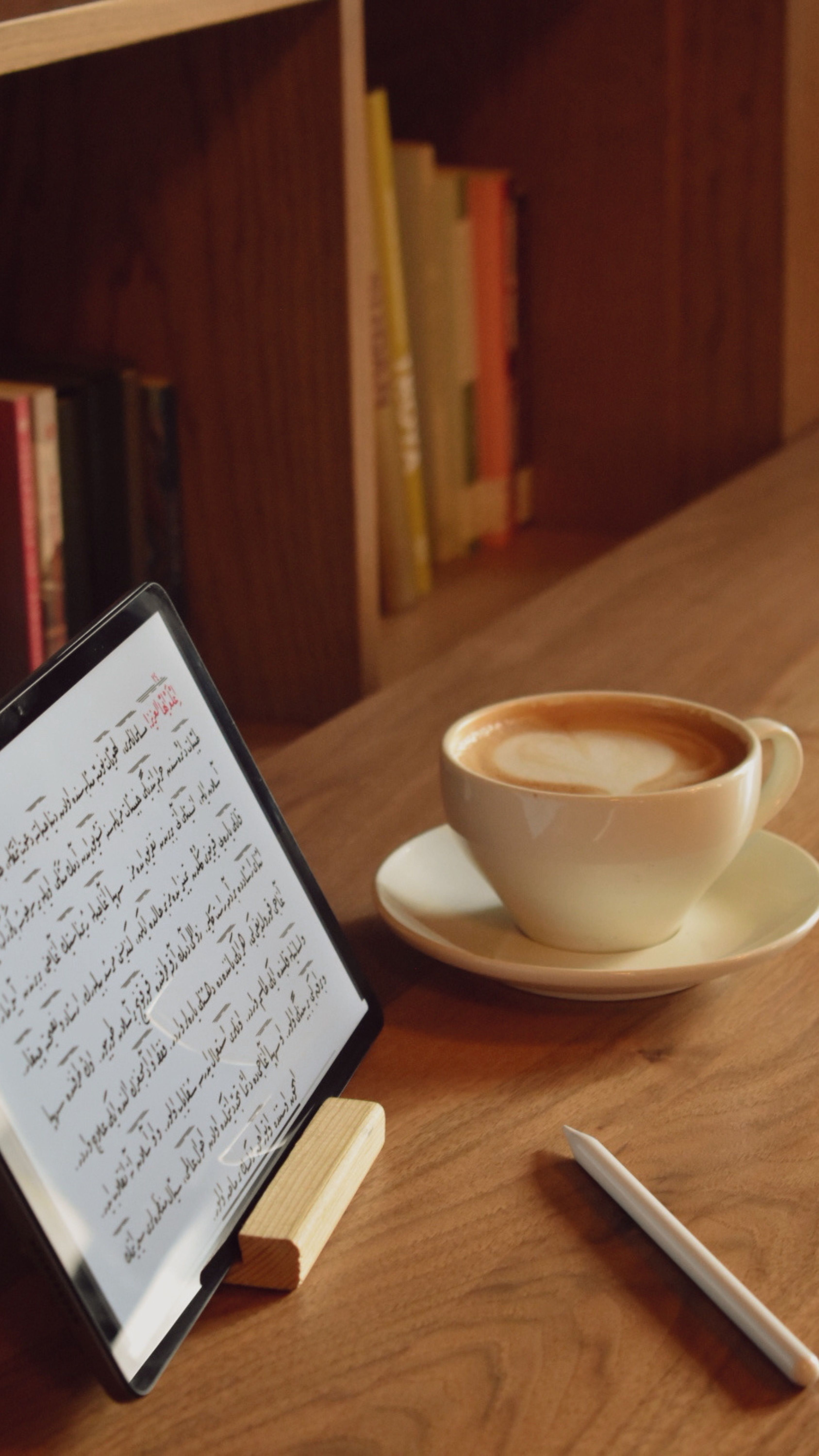Tablet displaying Arabic script beside a cup of coffee on a wooden desk.