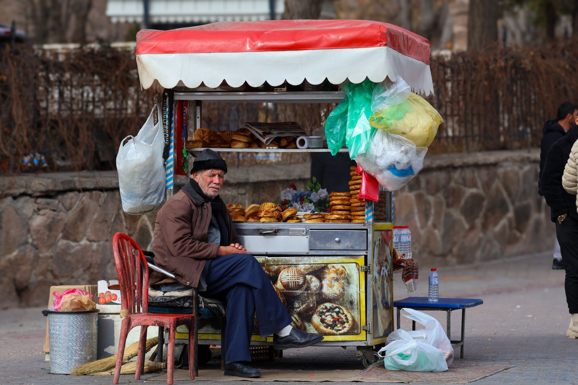 Elderly street vendor at a winter market stall selling pastries in an urban setting.