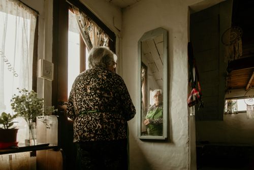 Free Elderly woman gazes at her reflection in a warm, cozy home setting with decor. Stock Photo