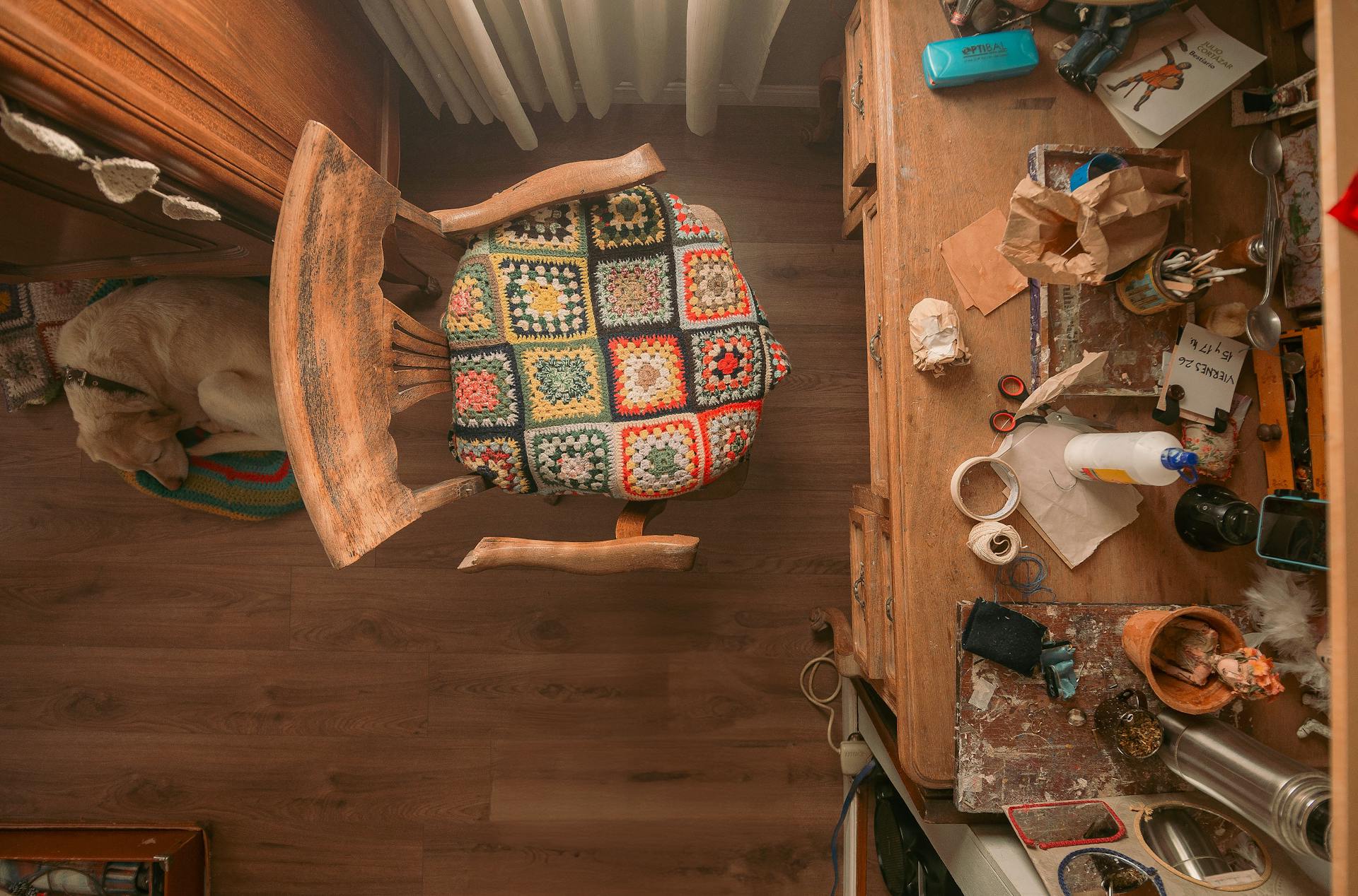 Top-down view of a craft room with a colorful quilted chair, cluttered desk, and a sleeping dog.