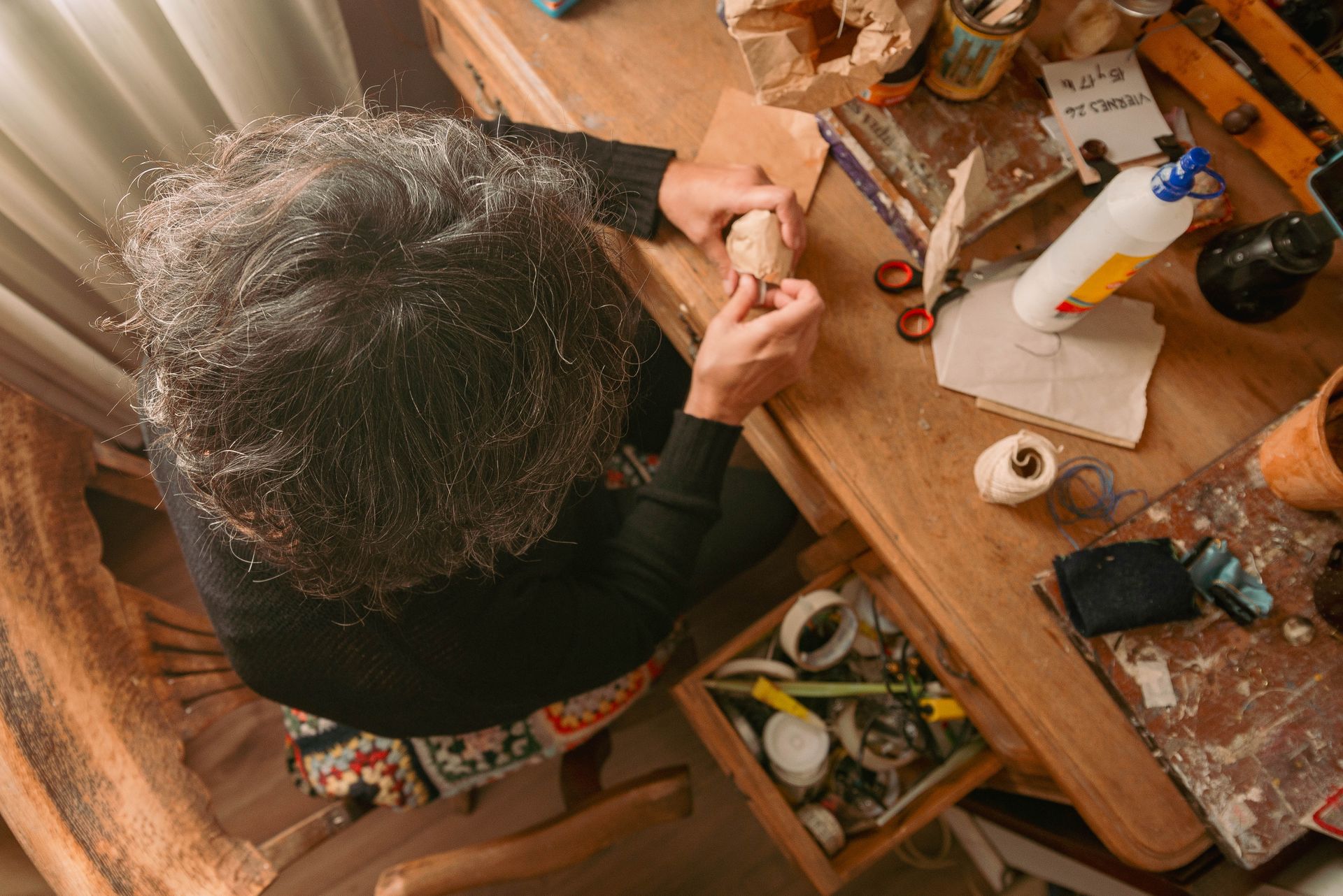 A person engaged in crafting, surrounded by tools and materials on a wooden desk.