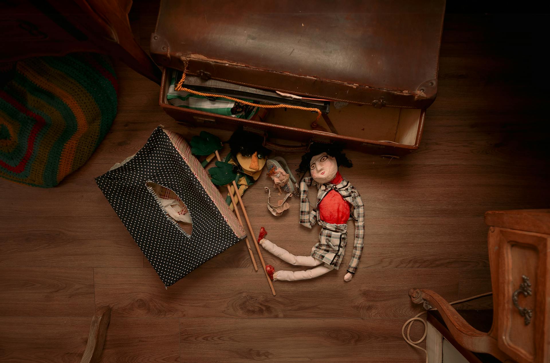 Artistic setup of vintage dolls and suitcase on wooden floor.