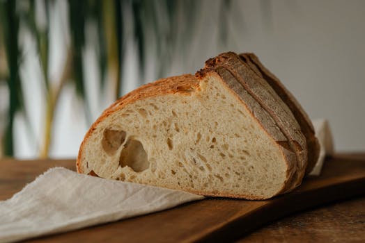 A slice of rustic artisan bread placed on a wooden board with warm lighting.