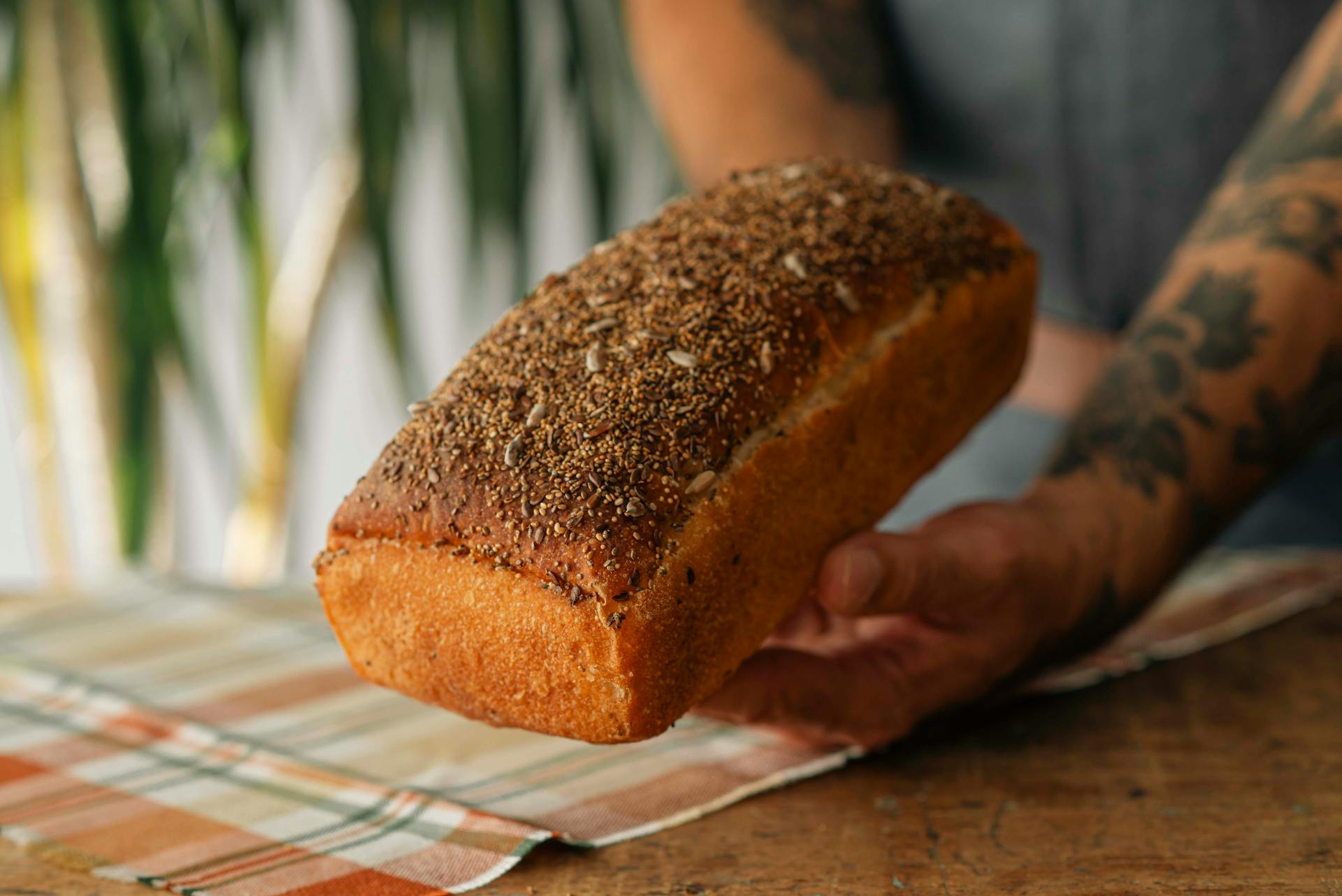 Freshly baked loaf of whole grain bread held by a tattooed artisan baker.