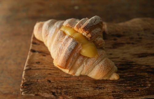 Free Close-up of a croissant with lemon filling on a rustic wooden board. Stock Photo