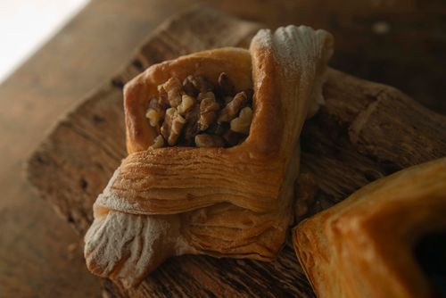 Free A close-up of a flaky walnut-filled puff pastry on a rustic wooden surface. Stock Photo