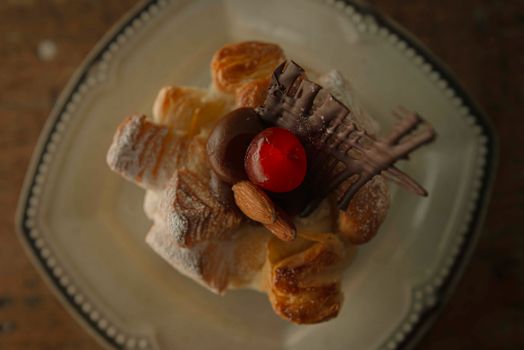 Close-up of a pastry topped with cherry, chocolate, and almonds on a plate.