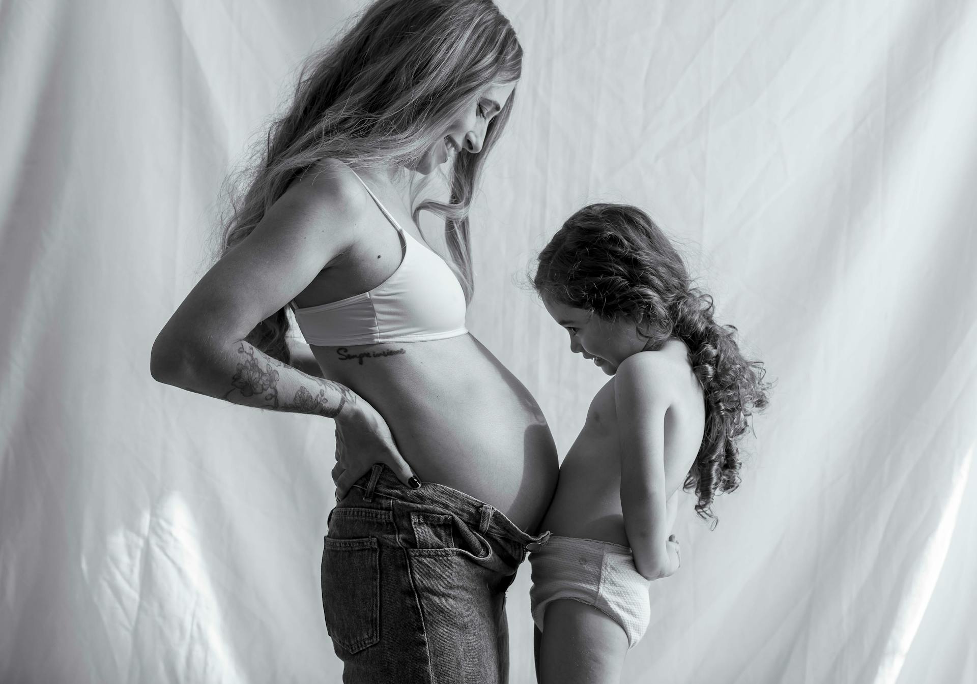 A heartwarming black and white image of a pregnant mother and her child sharing a tender moment indoors.