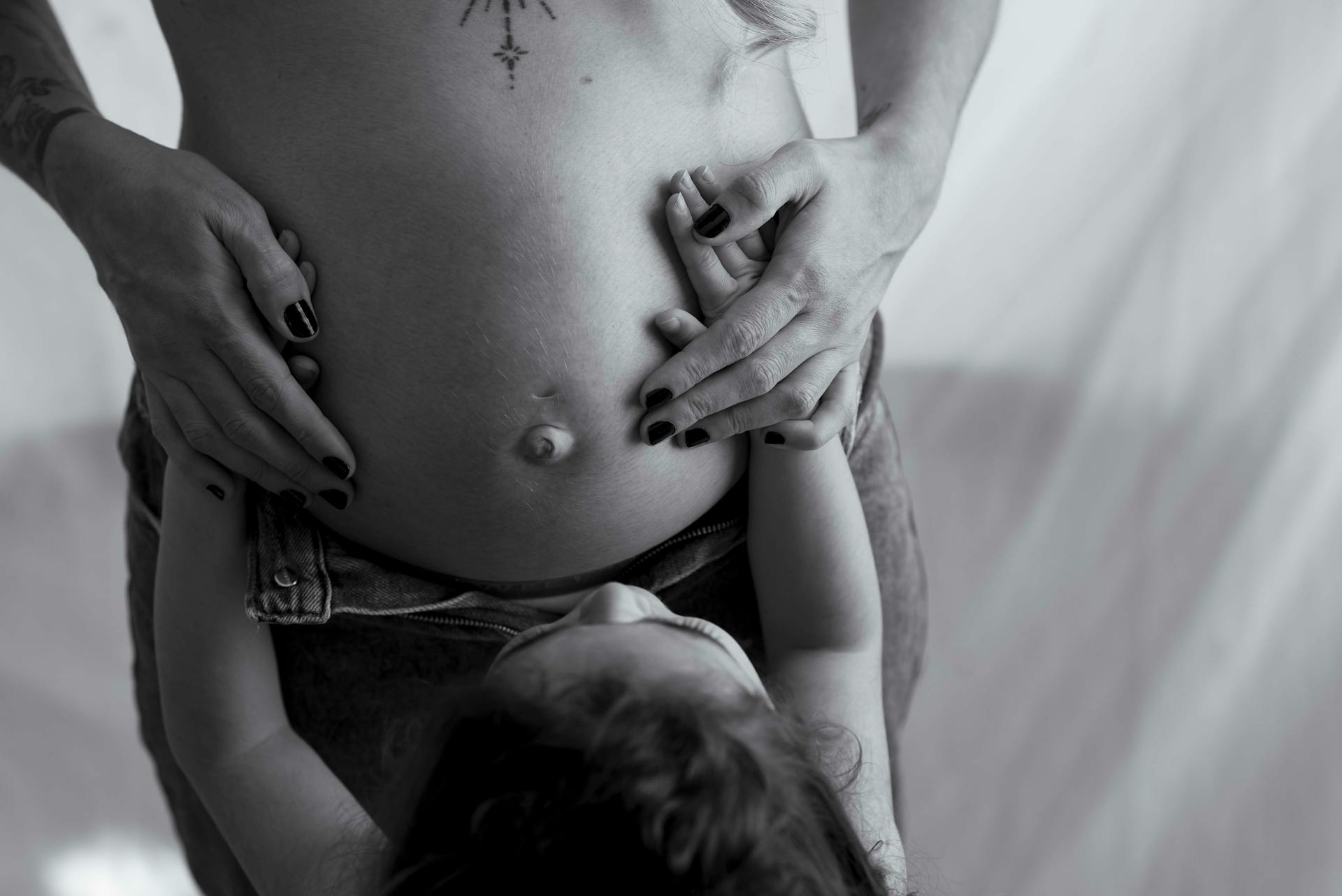 Black and white photo capturing a child's hands on a pregnant belly, symbolizing family bond.