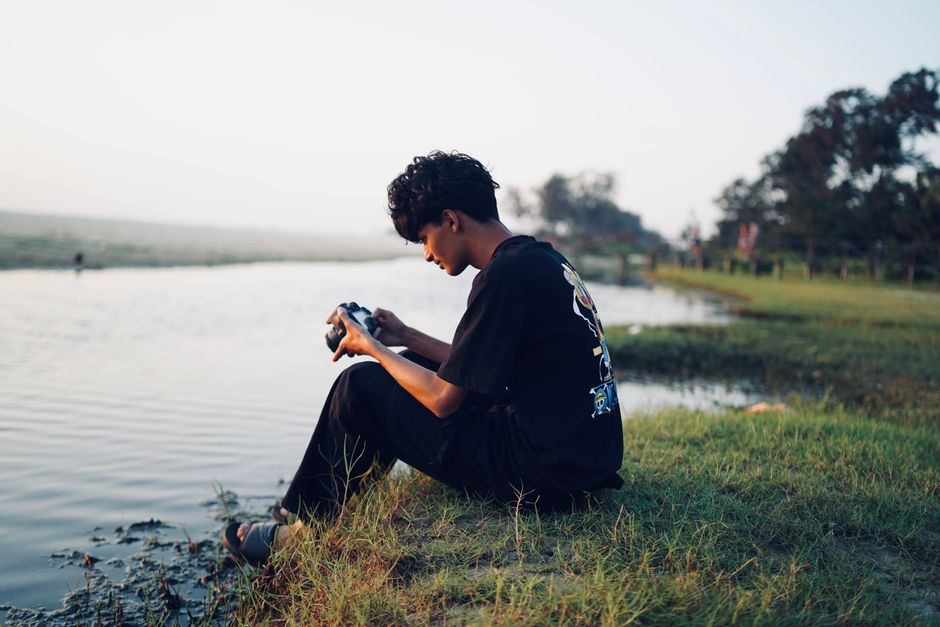 Youth exploring nature sitting by a calm riverbank during the day in GA, India, capturing moments.