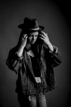A young woman poses in a denim jacket and fedora hat in a black and white portrait.