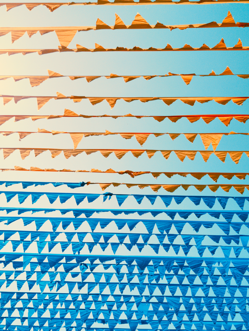 Free Vibrant triangular bunting flags strung across a sunny blue sky, creating a festive atmosphere. Stock Photo