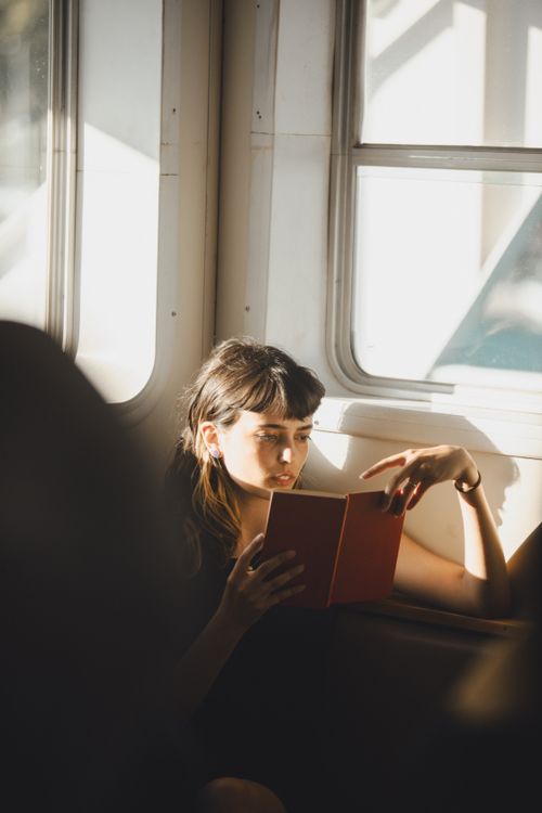 Free A woman engrossed in a book while traveling on an Istanbul ferry. Sunlight streams through the window. Stock Photo