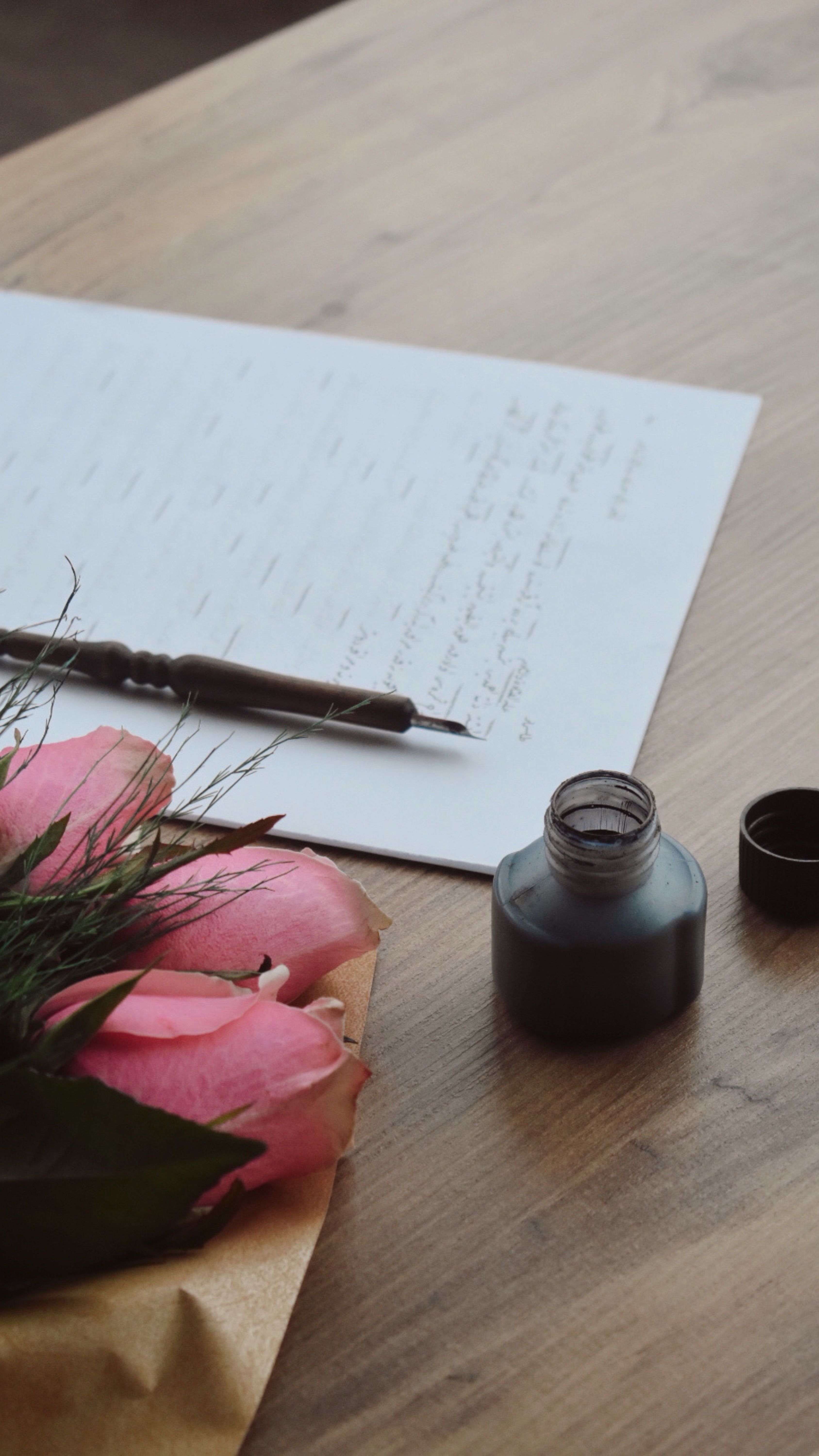Gratis Elegante scena di una lettera con rose rosa, calamaio e penna su un tavolo di legno. Foto a disposizione