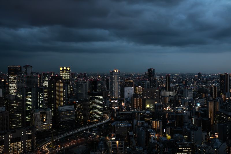 Dramatic Osaka skyline at twilight, showcasing illuminated skyscrapers against moody clouds.