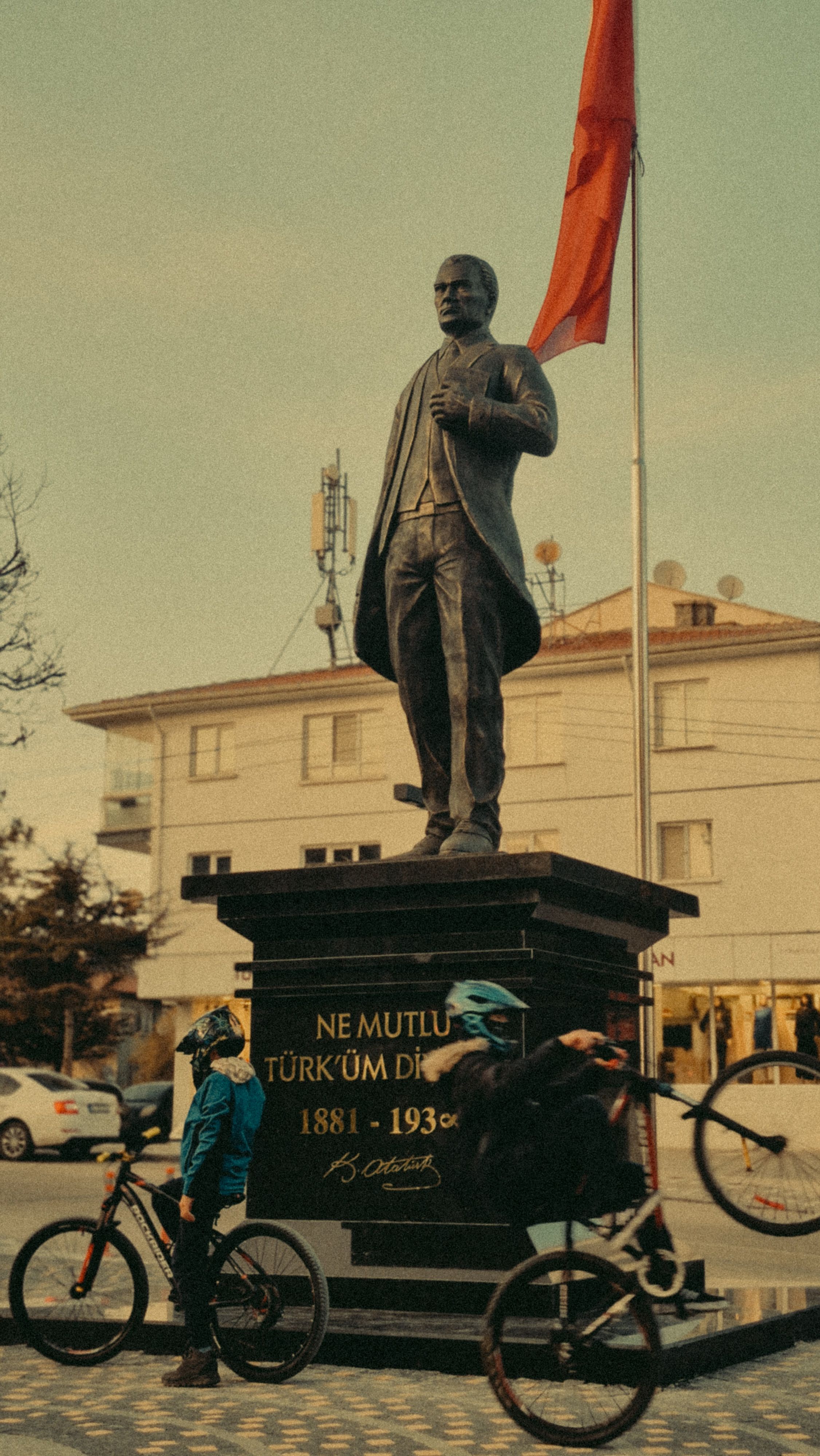 View of Ataturk statue in Turkish town with cyclists passing in front.