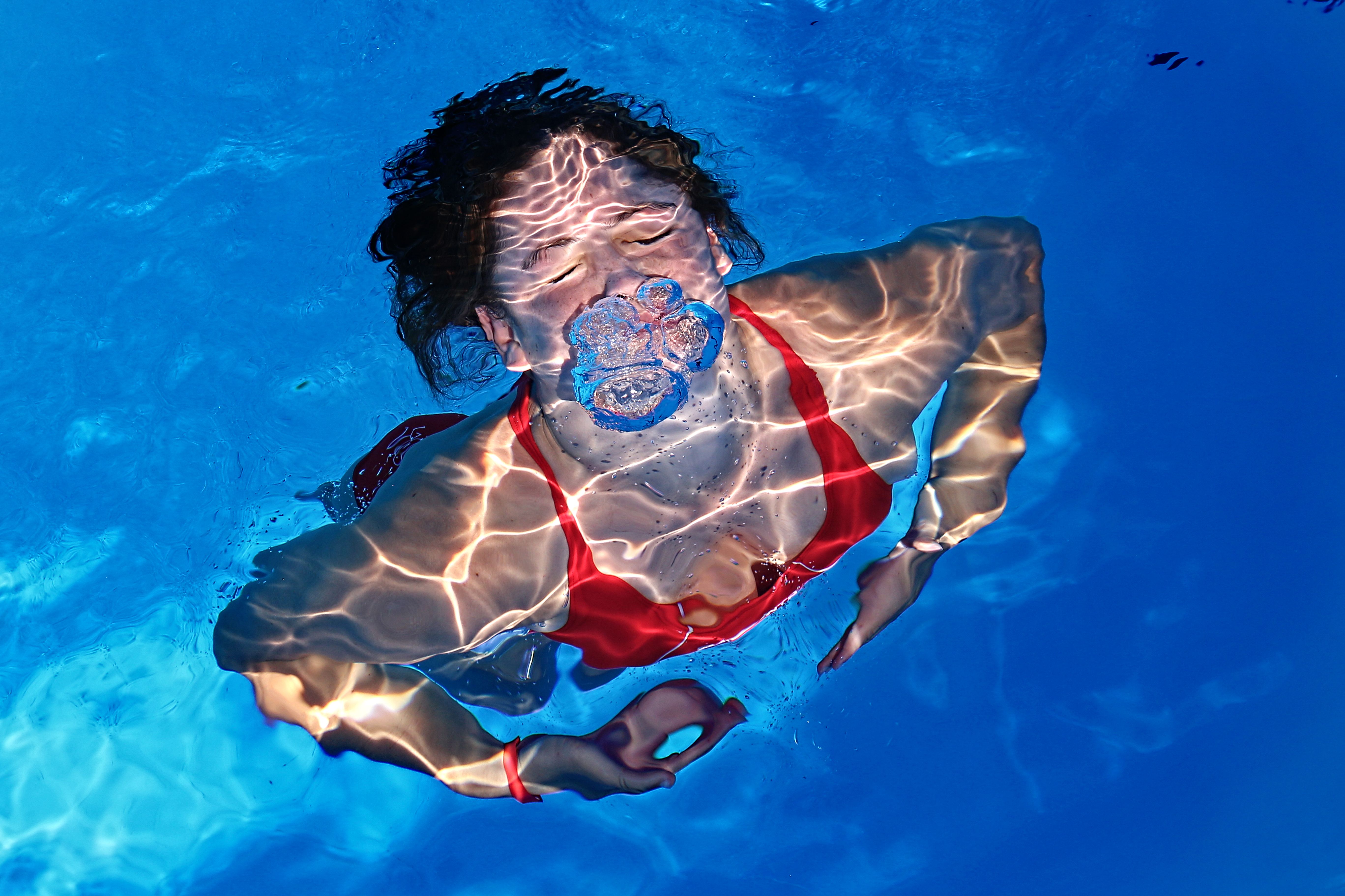 A woman in a red bikini swimming underwater, creating bubbles beneath the surface.