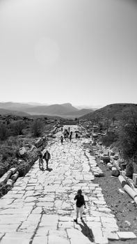 Black and white photo of people walking along an ancient stone road in a remote landscape.