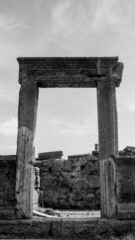 Black and white photo of an ancient stone archway among ruins.