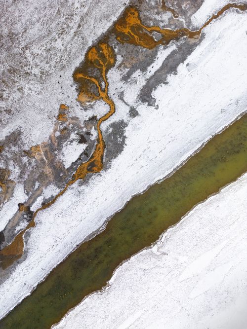 Free A striking aerial shot of snow, rocks, and a flowing river creating a natural pattern. Stock Photo
