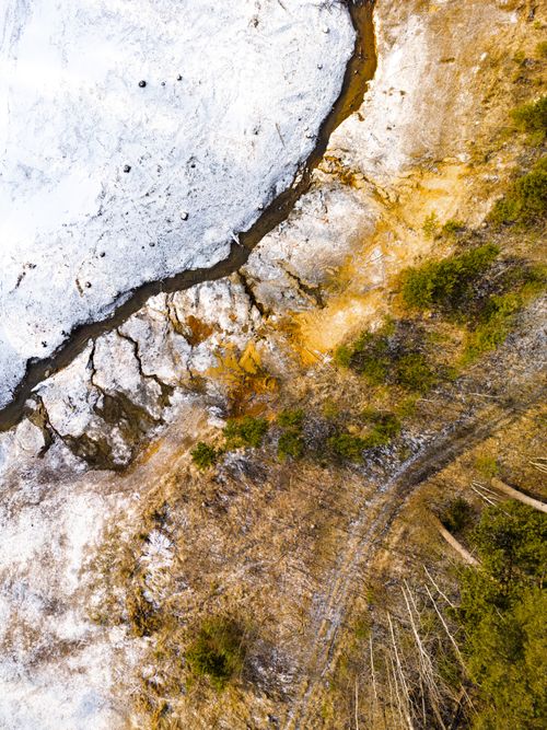 Free Aerial shot capturing frozen riverbank and sparse vegetation in winter. Stock Photo