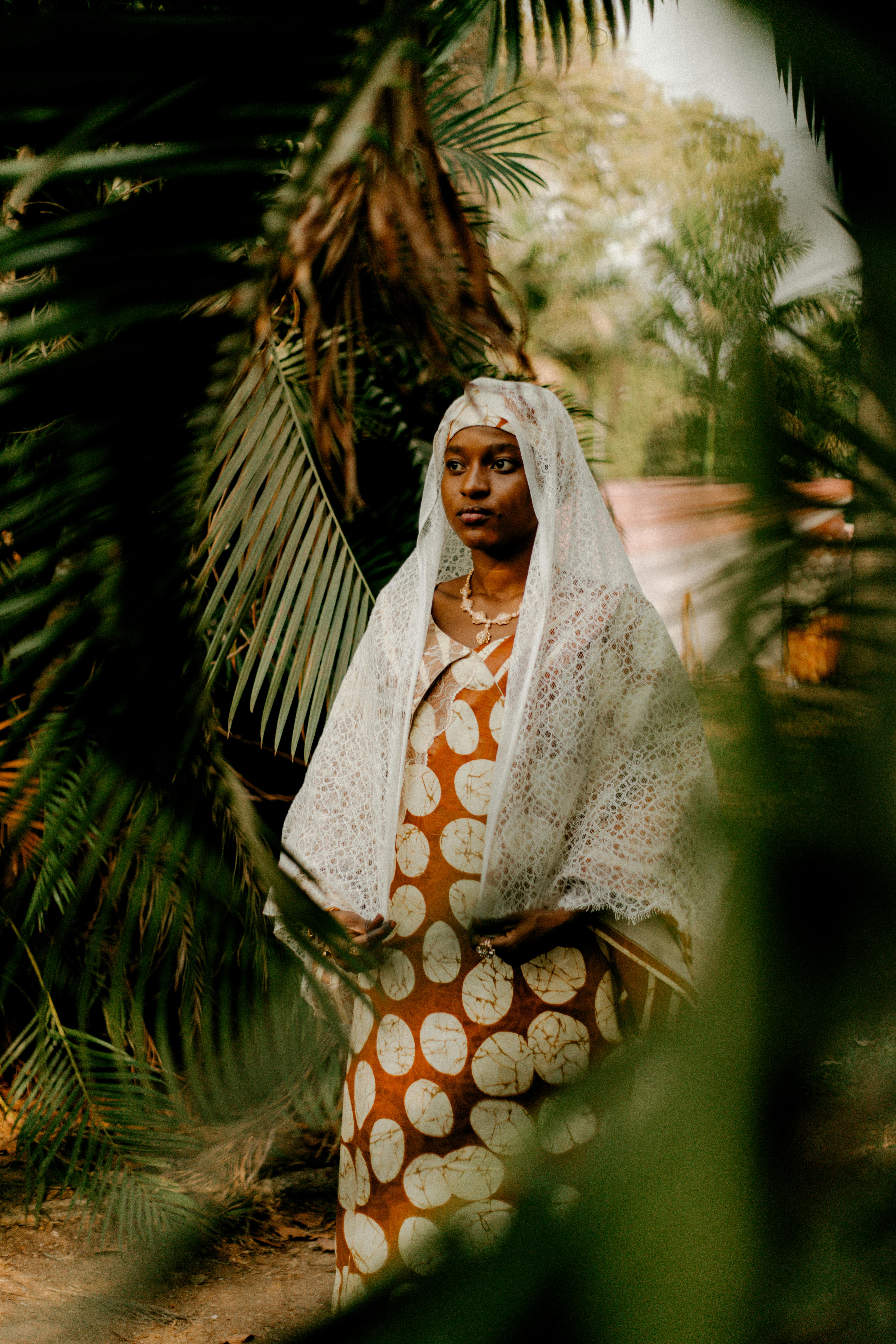 A woman in traditional attire stands gracefully amidst lush greenery.