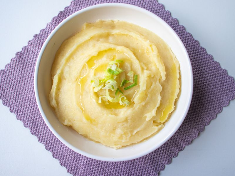 Top-down view of creamy mashed potatoes garnished with scallion in a white bowl.